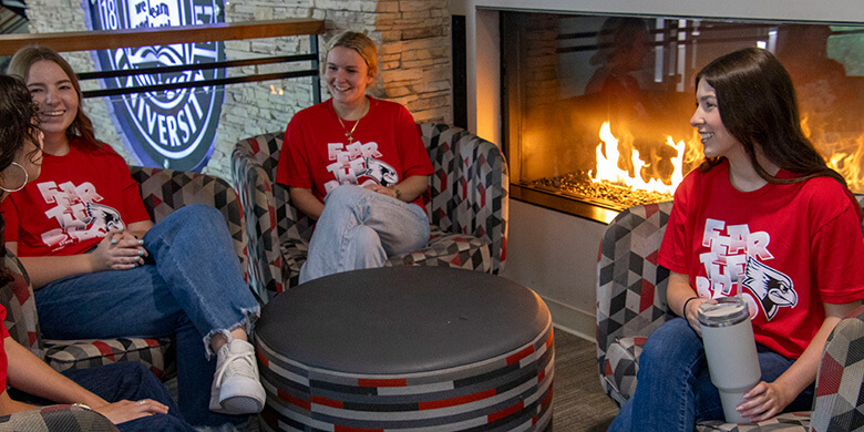 Four people in red Fear the Bird t-shirts sit and chat in a lounge area with a fireplace.
