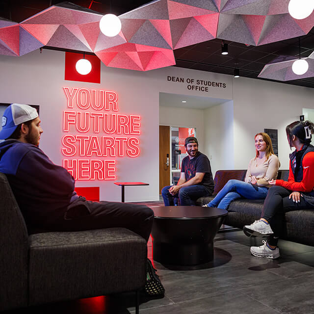 A modern student reception area with a neon sign reading 'YOUR FUTURE STARTS HERE' and geometric ceiling panels.