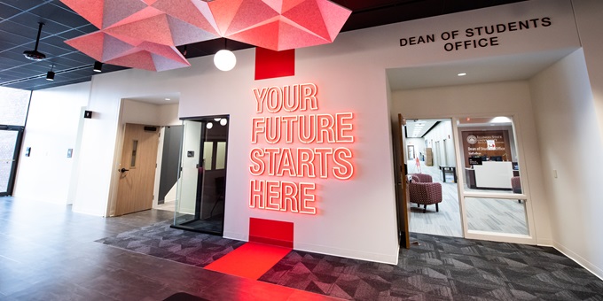 Modern seating area with a bird mascot mural, geometric light fixtures, and a large digital display